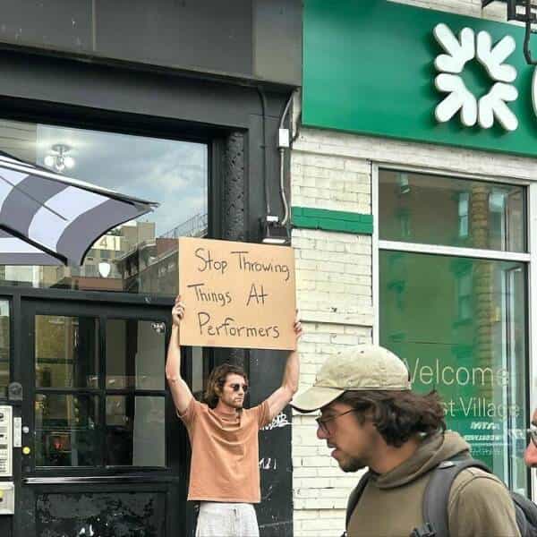 dude with a sign Stop Throwing Things At € Performers