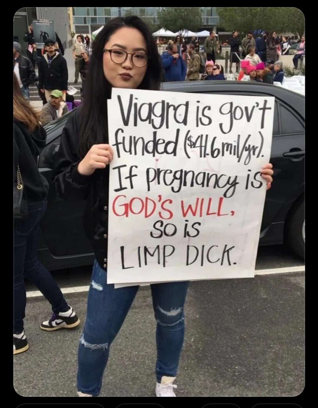 Woman holding sign at protest that reads: "Viagra is gov’t funded ($41.6mil/yr). If pregnancy is GOD’S WILL, so is LIMP DICK."