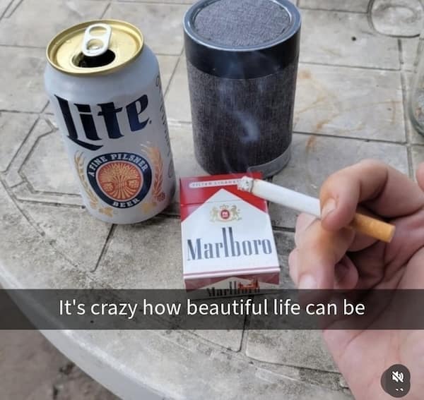 Marlboro cigarette, beer, and speaker on table with caption “It's crazy how beautiful life can be”