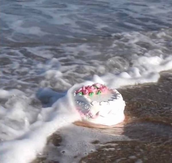 Decorated cake washing ashore with ocean waves on the beach.