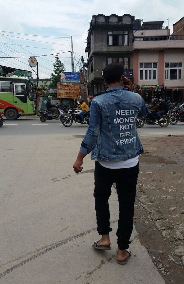 Man walking on the street wearing a denim jacket with bold text on the back.