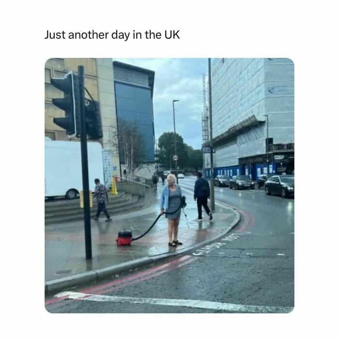 Woman with vacuum cleaner in rainy UK street.