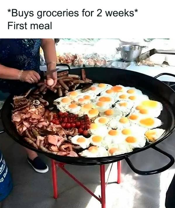 Giant skillet filled with eggs, bacon, and sausages being cooked outdoors.