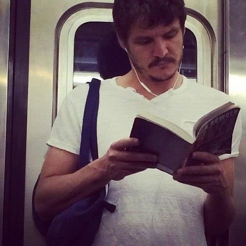 Man reading a book on subway while wearing earbuds