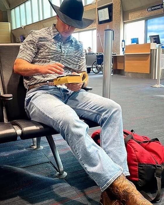 Cowboy reading a book at airport terminal in boots and hat