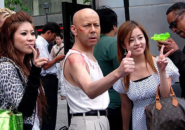 Man dressed like Bruce Willis’s Die Hard character posing with fans on the street.