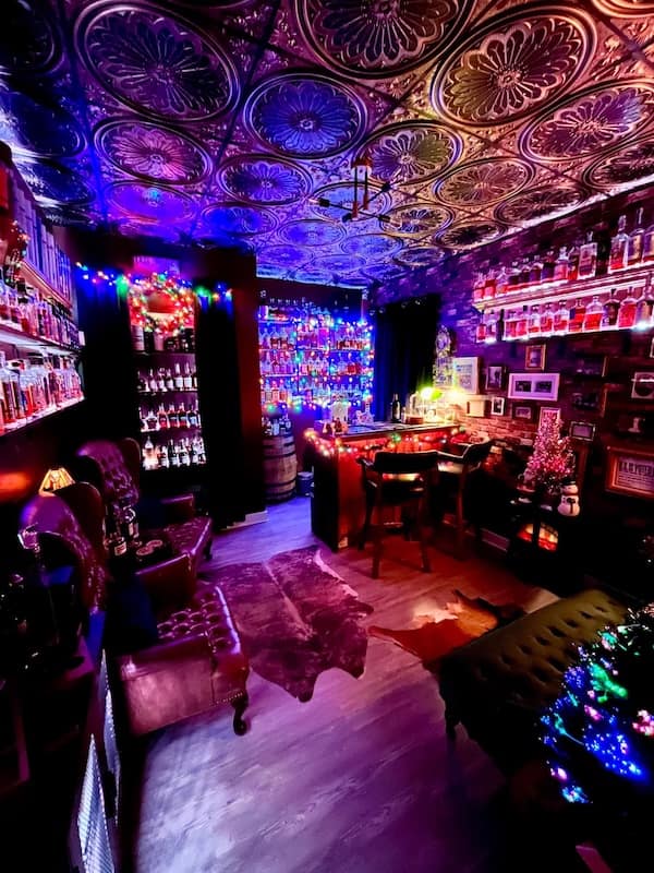 Dark neon bar room with vintage ceiling tiles and colorful LED bottle shelves