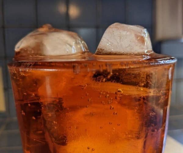 Satisfying photo of two crystal-clear ice cubes rising above a glass of carbonated amber soda, creating a pleasing balance and refreshing look.