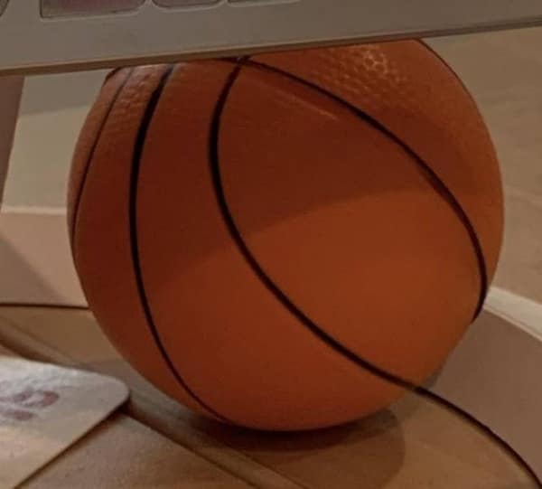 Satisfying photo of a basketball tightly wedged under a computer monitor stand, fitting the space so precisely it almost looks intentional.
