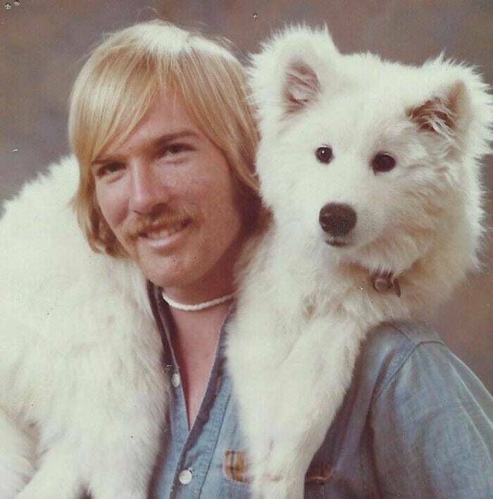 Blonde man with mustache poses with fluffy white dog draped around his shoulders