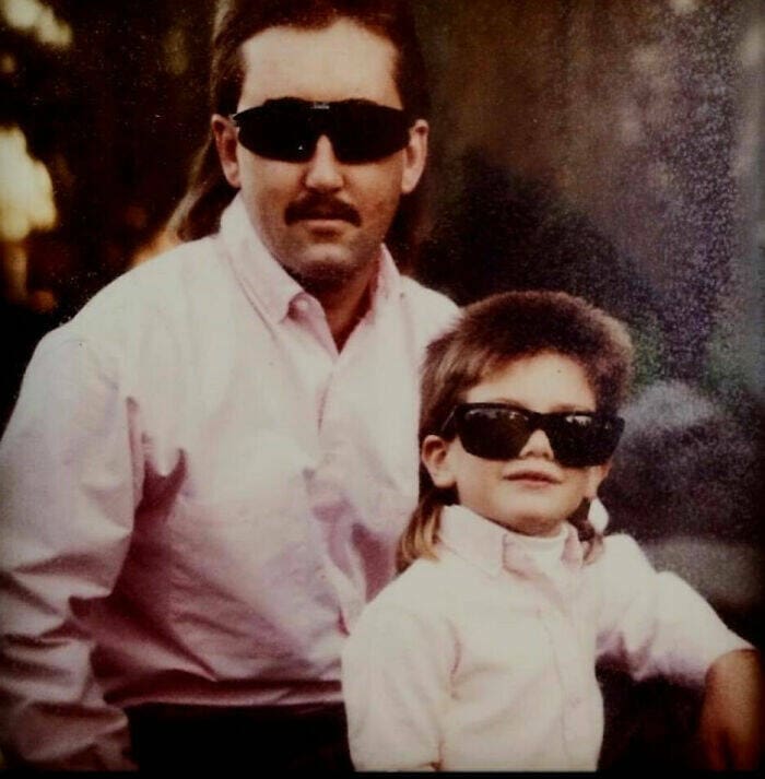 Father and young son in matching sunglasses and mullets pose together