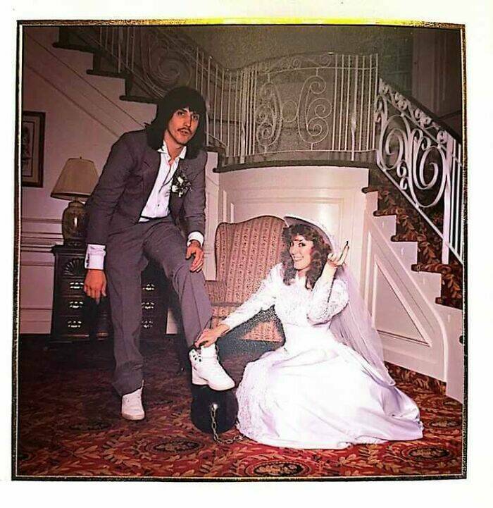 Bride in wedding dress chaining groom’s foot to a ball during photo shoot