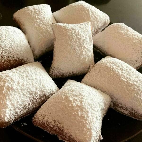 Plate piled with powdered-sugar-covered beignets.