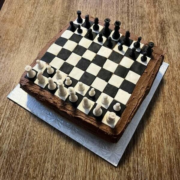 Chessboard cake with edible black and white fondant pieces arranged for play.
