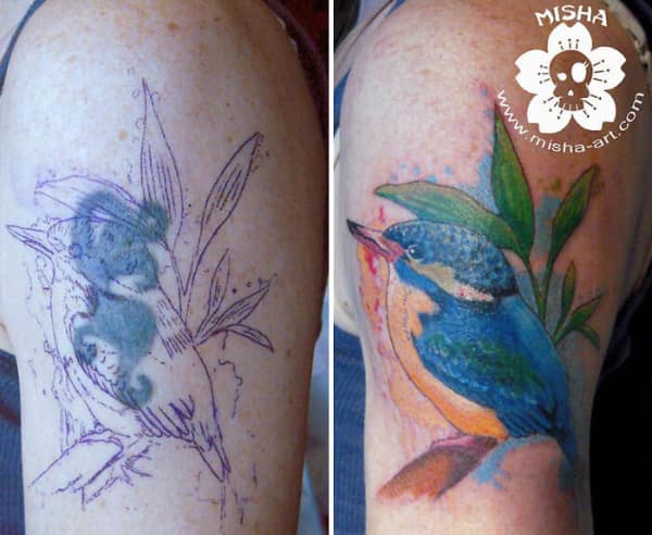 Vibrant kingfisher bird tattoo cover up with watercolor-style background and green foliage.