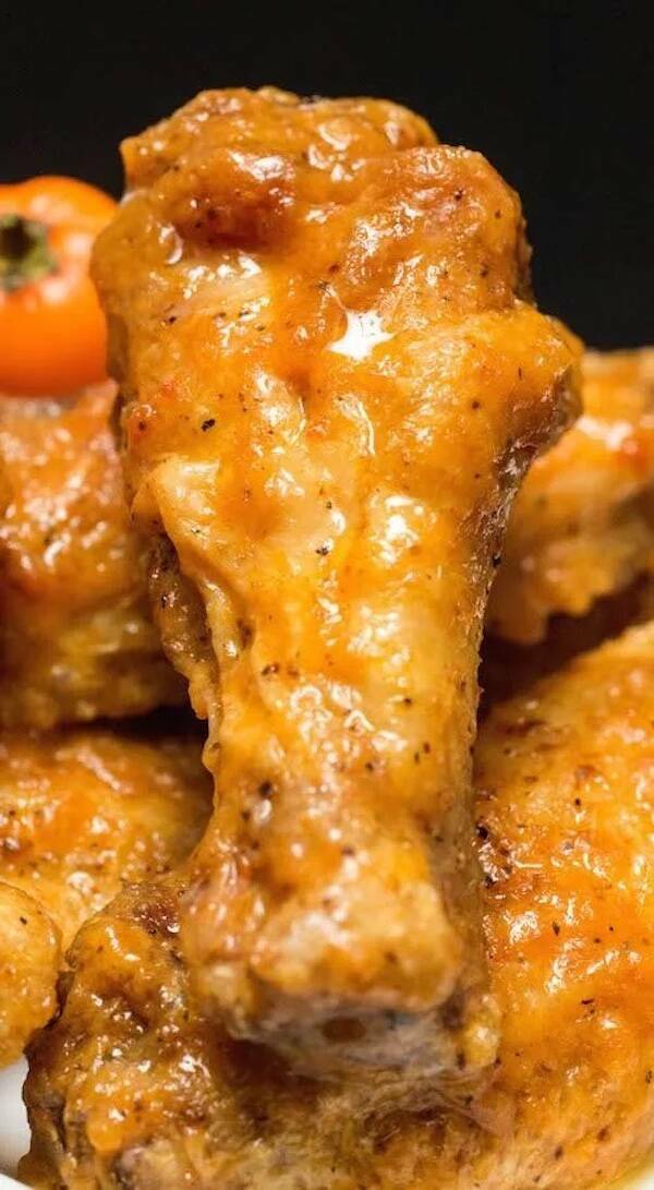 Extreme close-up of a saucy chicken wing drumette glazed in orange pepper sauce