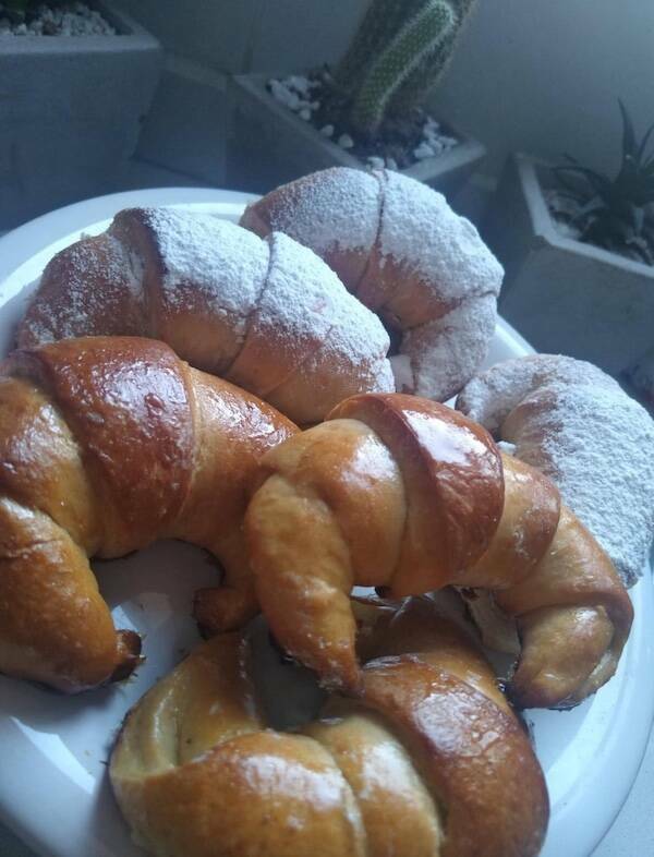Plate of crescent rolls, some dusted with powdered sugar, others glossy with glaze
