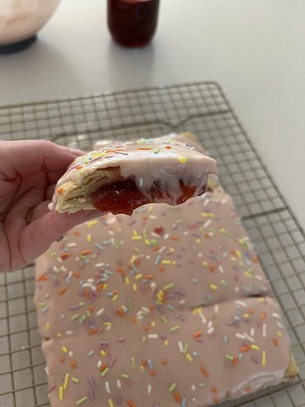 Hand holding a strawberry-filled homemade Pop-Tart with pink icing and rainbow sprinkles
