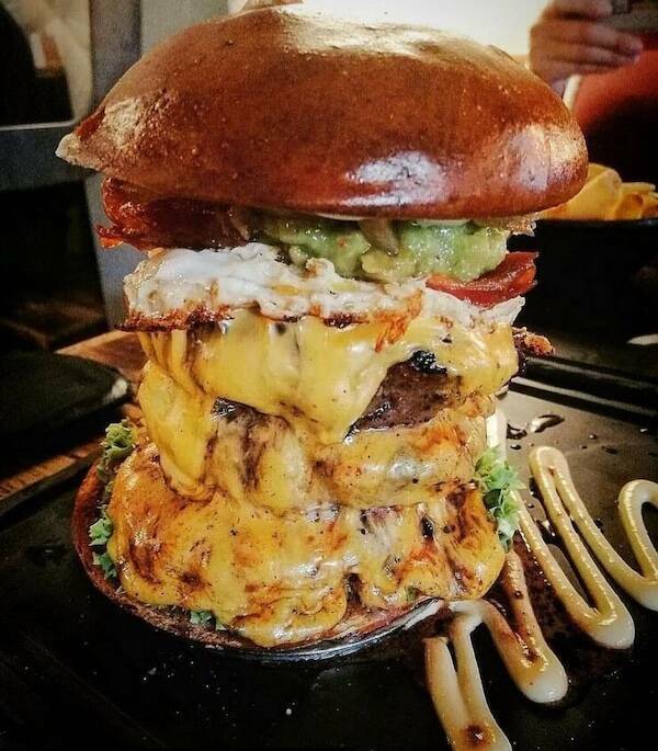 Towering cheeseburger with bacon, fried egg, guacamole, and melted cheese spilling down
