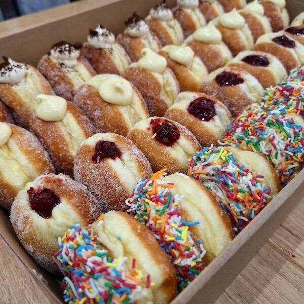 Box of assorted filled doughnuts—custard, jam, and sprinkle-covered varieties in rows