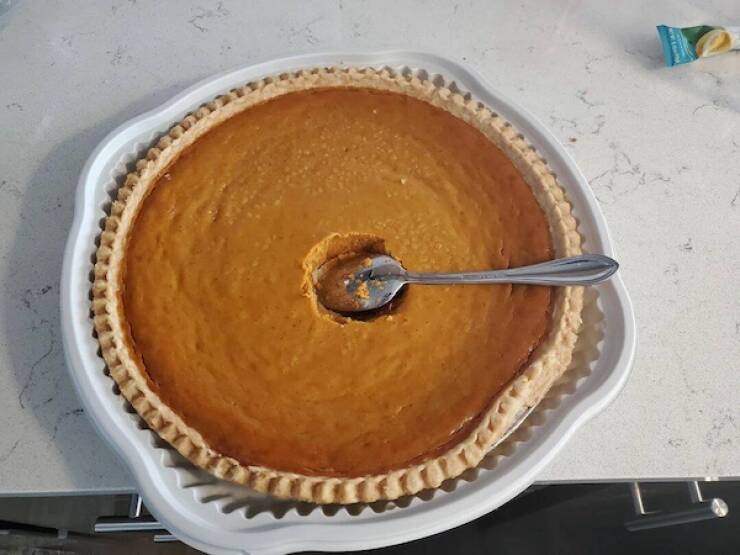 Whole pumpkin pie with a spoonful scooped from the center, spoon left in the pie.