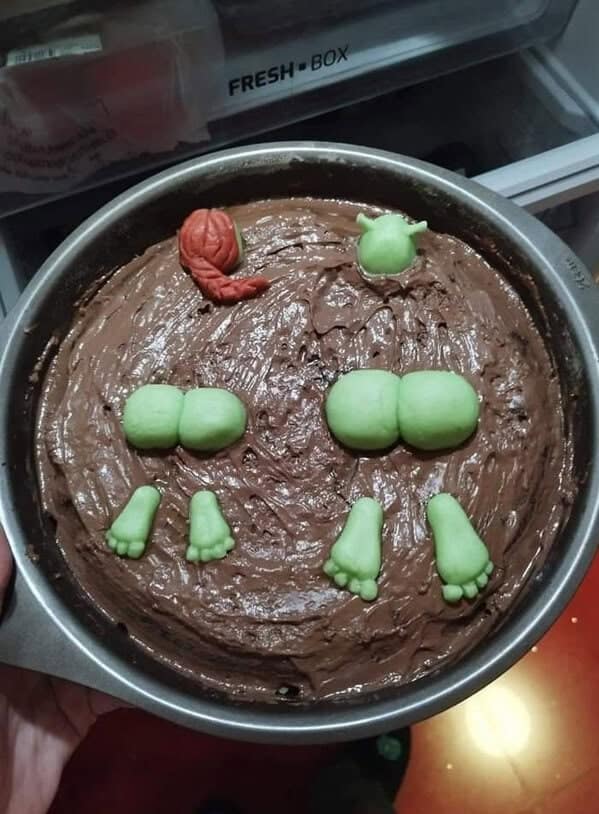 A chocolate cake decorated to resemble Shrek and Fiona submerged face-first, with their green fondant feet and butts sticking out.