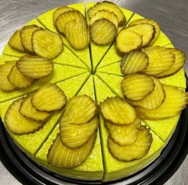 A bright yellow cheesecake or pie topped with symmetrical piles of dill pickle slices.