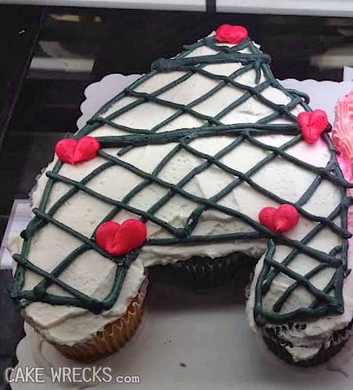 A cupcake cake shaped like a heart or tree, iced in a web of green lines and dotted with red hearts.