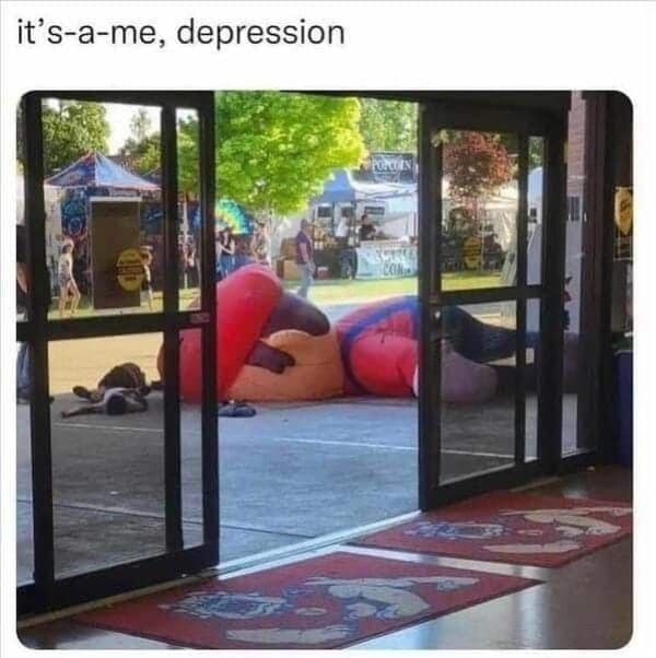 A deflated Mario inflatable lying on the ground outside a building, captioned “it’s-a-me, depression.”