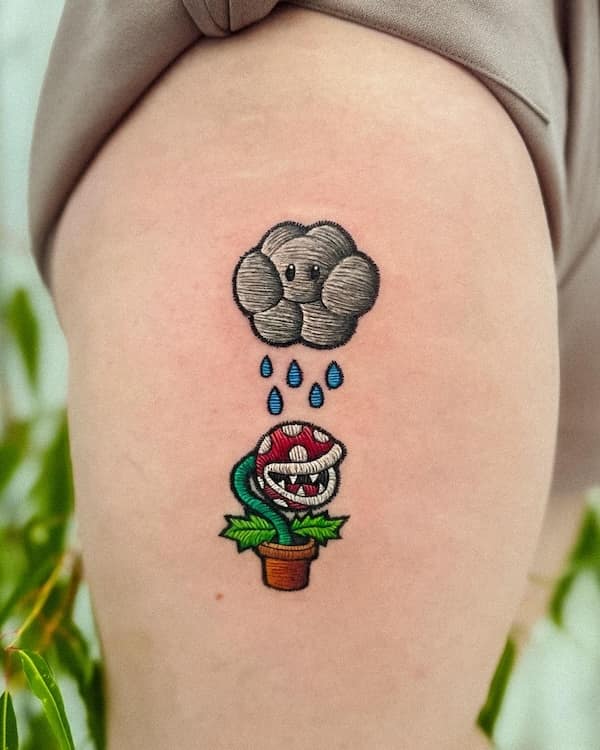 Tiny embroidered-patch tattoo of a cute gray rain cloud watering a Mario piranha plant on a thigh.