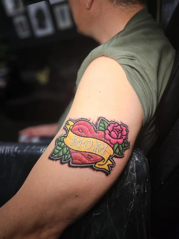 Traditional “MOM” heart and banner rendered to look like a stitched fabric patch on the upper arm.