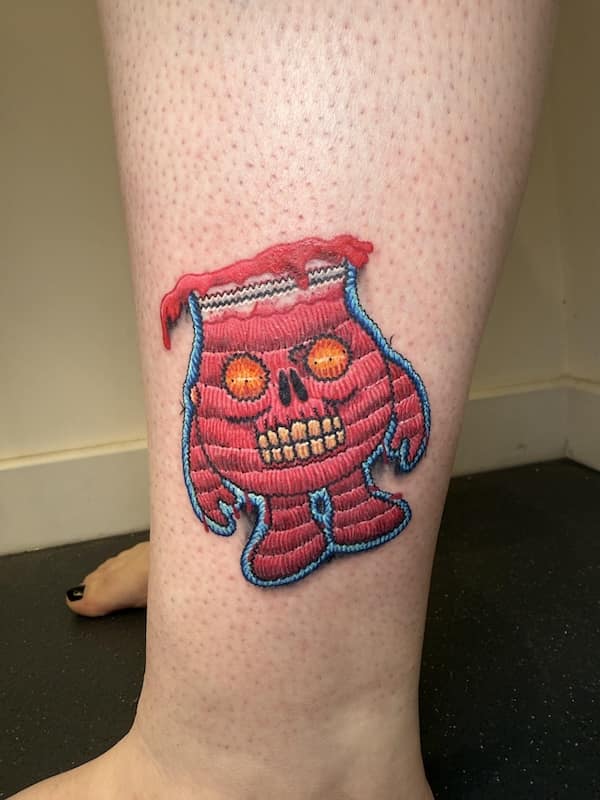 Bright pink stitched monster with skull face and glowing eyes, done as a small patch-style tattoo on a leg.