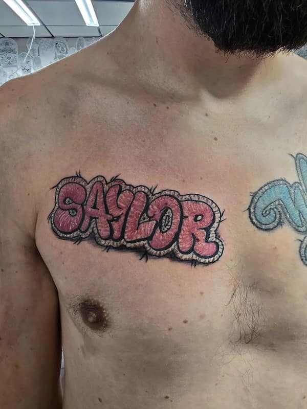 Bold pink “SAYLOR” name across chest in puffy stitched bubble letters with little loose threads.