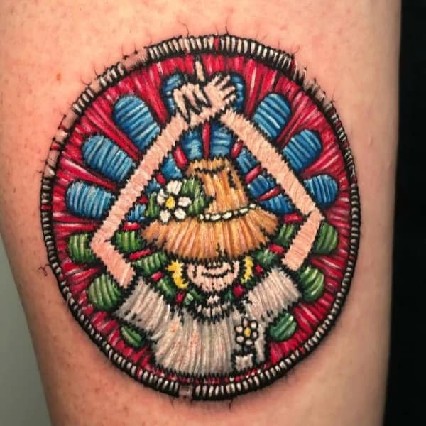 Circular patch-style tattoo of a straw-hat character raising arms amid red and blue rosette background.