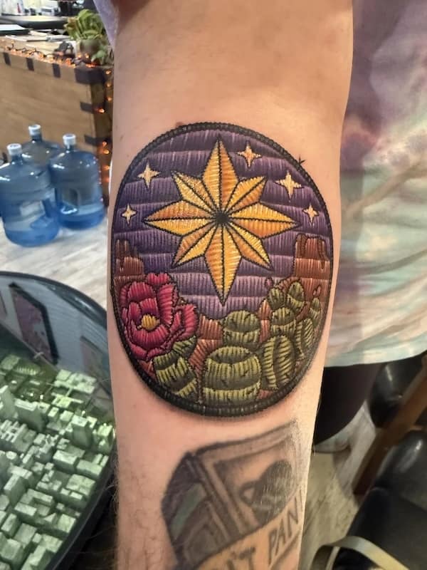 Oval desert scene with golden compass star, cacti and flowers, shaded to look like sewn threads.