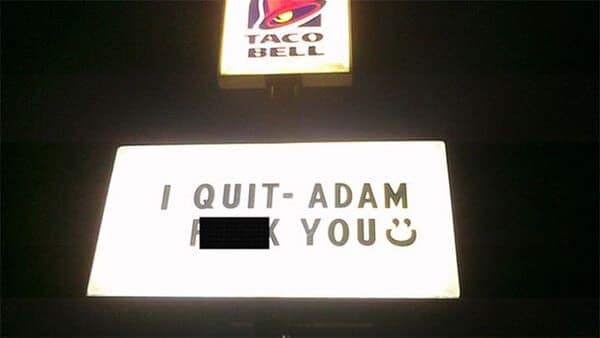 A Taco Bell sign at night reading “I QUIT - ADAM F*** YOU :)”.