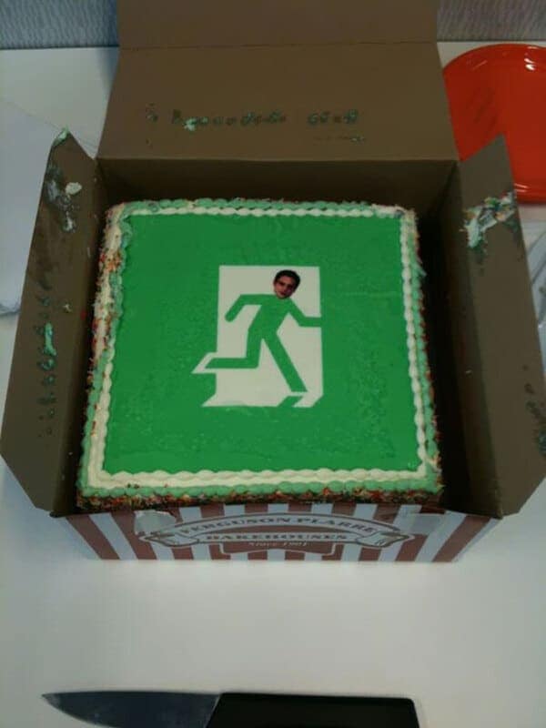 A green frosted cake showing an emergency exit sign with a man’s face edited onto the running figure.