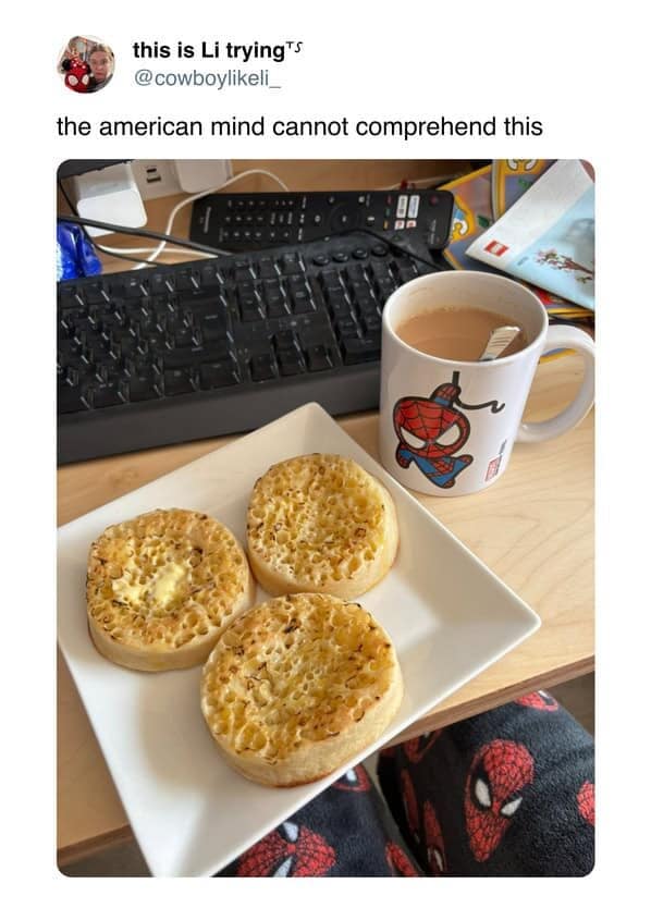 Plate of three crumpets with butter next to a mug of tea on a desk