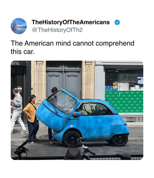 A compact blue microcar with a front-hinged door on a European street.