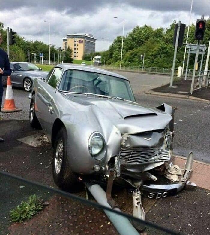 A classic silver Aston Martin DB5 sports car with its front end completely smashed.
