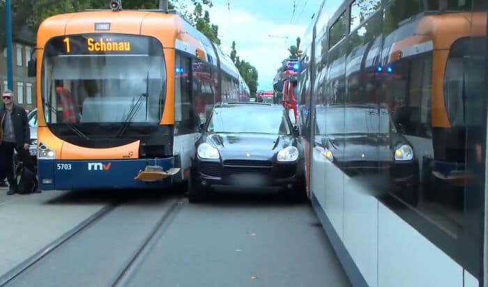 A black Porsche Cayenne luxury SUV wedged and stuck between two city trams.
