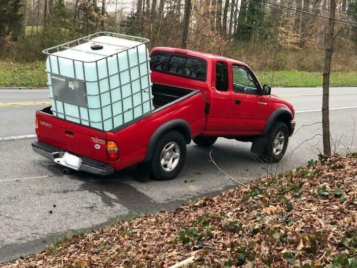 A small red pickup truck's suspension squatting under the immense weight of a water tank.