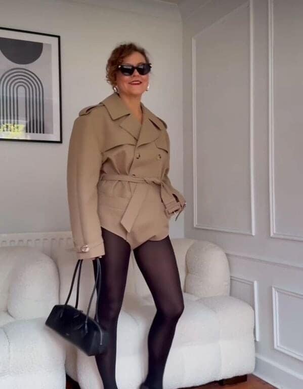 A fashion fail of a woman wearing a very short cropped trench coat like a romper with tights.
