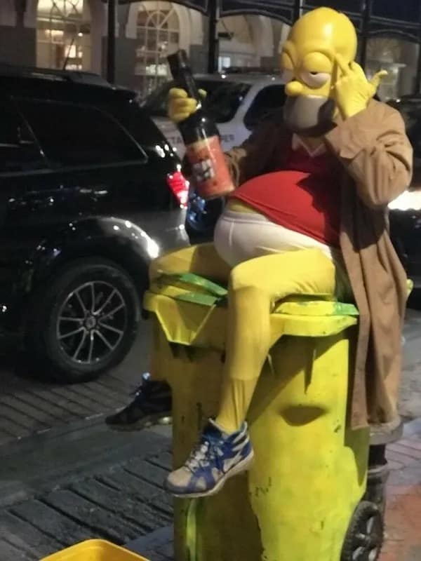 Man in Homer Simpson costume sitting on garbage bin