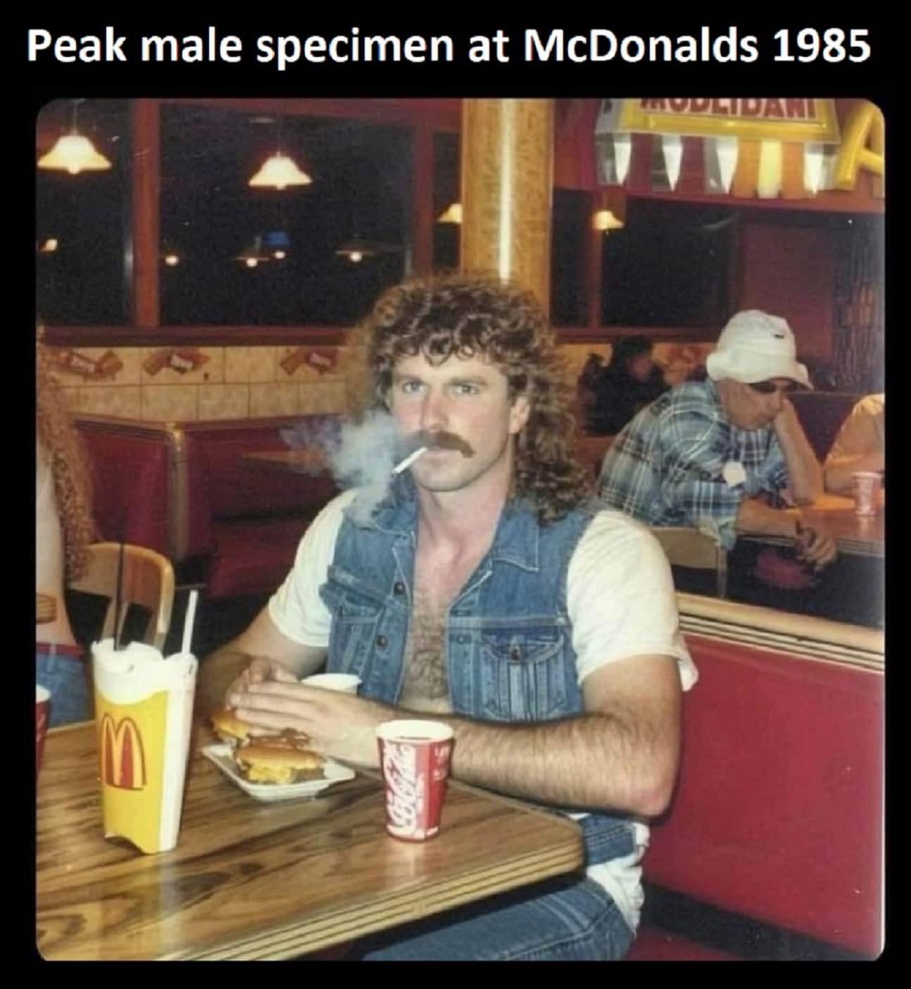 A funny pic of a man with a mullet smoking in a McDonald's restaurant in 1985.