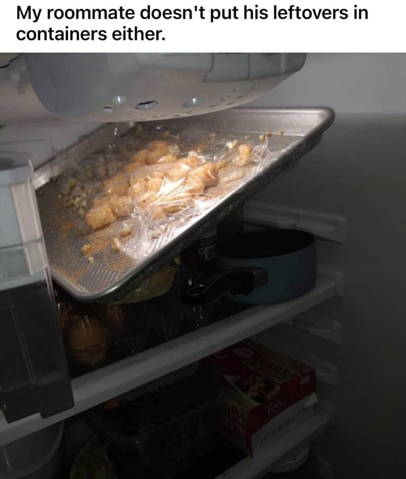 A large baking sheet of leftovers is wedged diagonally into a refrigerator without a container.