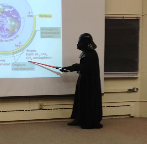 Instructor dressed as Darth Vader using a red lightsaber pointer during a science lecture