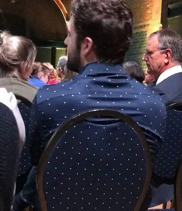 Man in navy polka-dot shirt seated before a chair with matching dots.
