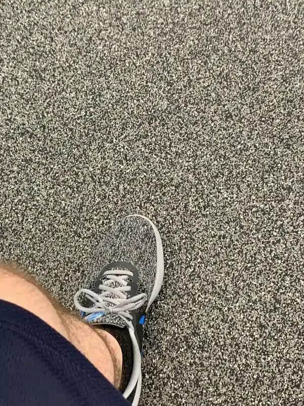 Gray knit sneaker on speckled carpet, nearly indistinguishable from the floor.