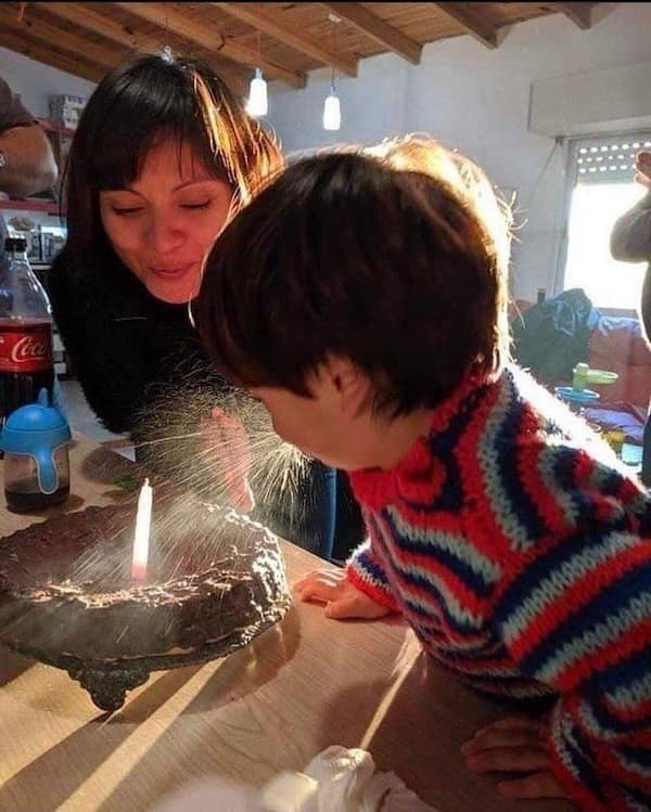 Child sprays spit while blowing out a birthday candle beside mom.